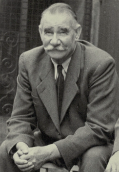 Schwarz-Weiß Porträt eines älterer Mann im Anzug sitzt draußen und schaut ruhig in die Kamera.